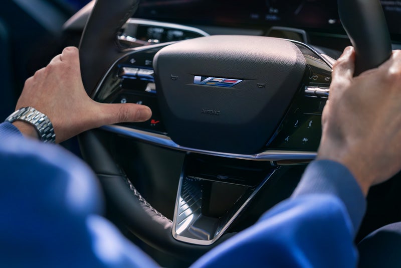 Close-up of a Man About to Press the V-Button on the 2026 OPTIQ-V Steering Wheel | Cadillac of Jackson in Ridgeland MS